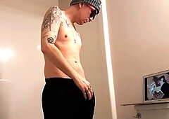 Horny inked dude strokes his throbbing young cock in the shower while watching hot milf porn