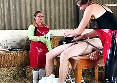 Nurse in red apron administers enema to naked patient in barn medical roleplay