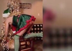 Carlie Vixen is home alone decorating her Christmas tree in a hot little green elf dress, her small green strap flashing underneath the short petticoa