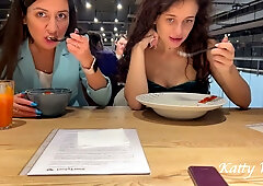 Katty West and a curly-haired woman dine bare beneath the table in a public restaurant